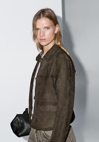 Brown suede jacket with a collared neck and button-up front. Additional features include side pockets and a slightly fitted design.