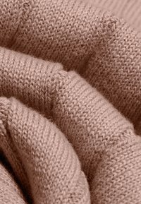 Tissu tricoté doux rose clair avec des coutures visibles et une surface texturée, légèrement duveteuse en gros plan.