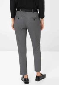 Hosen mit Hahnentrittmuster und schmaler Passform, ausgestattet mit Gesäßtaschen und einem schwarzen Bund. Tragen Sie dazu schwarze Slipper.