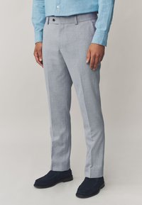Pantaloni grigi chiaro sartoriali con una texture sottile, davanti piatto e gambe dritte. Abbinati a mocassini in suede blu scuro.