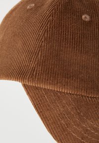 Detailný záber hnedého kordurového baseballového klobúka s textúrovanou tkaninou a prešitými detailmi na okraji a paneloch.