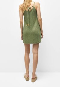 Robe tricotée verte avec un design fluide, des bretelles ajustables et une attache nouée dans le dos. Portée avec des sandales compensées à dessus à motif.