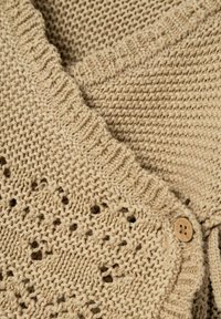 Maglione beige lavorato a maglia con un motivo testurizzato e un bottone di legno. Presenta un colletto a coste e dettagli in maglia aperta lungo l'orlo.