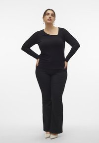 Top negro de manga larga con textura acanalada y escote cuadrado, combinado con pantalones negros acampanados y tacones beige puntiagudos. Diseño simple, textura suave.