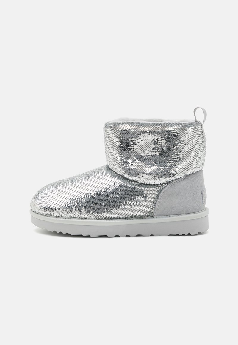 Bottine courte argentée à sequins avec haut replié, talon en daim gris clair, semelle blanche et languette sur un fond uni.