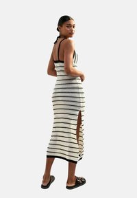Abito a maglia a righe in bianco e nero, con una silhouette aderente, spacco laterale e sottili spalline nere. Indossato con sandali neri.