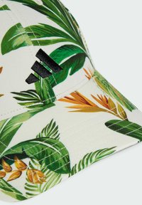 Gorra blanca con vibrantes patrones de hojas tropicales en verde y naranja. Presenta un logo negro en la parte frontal y detalles de costura visibles.