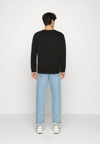 Sudadera negra de mangas largas, con cuello redondo, combinada con jeans de mezclilla azul claro. La tela parece suave y de corte relajado.