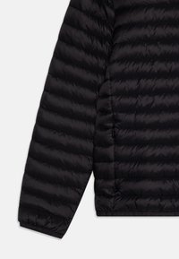 Giacca nera imbottita con motivo a righe orizzontali, texture liscia e dettaglio con zip sul lato inferiore. Maniche lunghe con polsini aderenti.