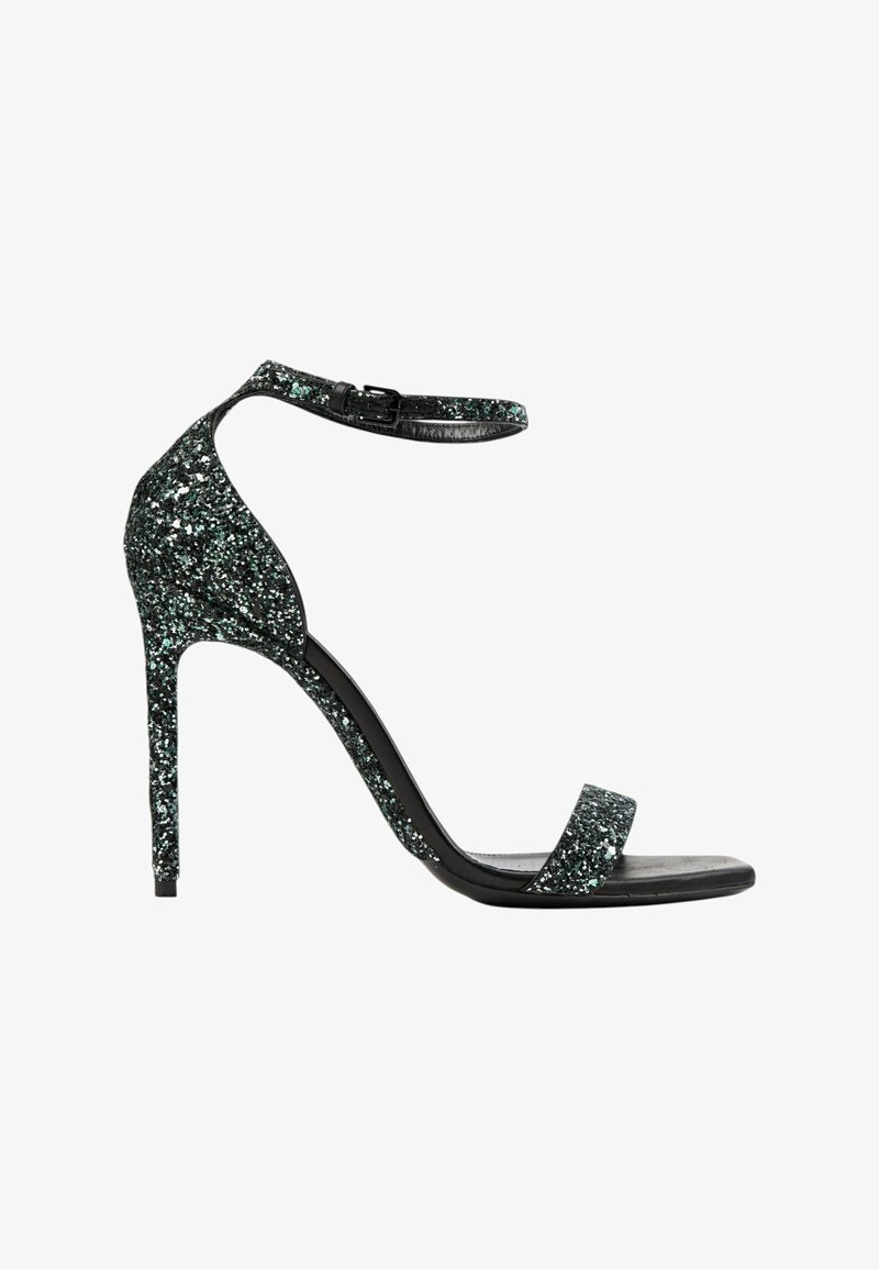 Sandale à talon haut noire avec détails scintillants, fine bride de cheville avec boucle et bride unique sur les orteils, sur fond blanc.