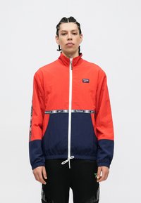 Punased ja tumesinised tuulejoped kõrge kaelusega, elastsete mansettidega, valge tõmbluku ning Reebok'i logoga rinnal ja triipudega varrukaid.