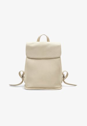 Zaino in pelle crema con forma strutturata, patta pieghevole e cinghie laterali regolabili. Texture liscia con accenti hardware minimi.