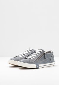 Sneakers in pelle grigia con lacci bianchi, una cerniera laterale, superficie testurizzata e logo sul tallone. Presentano una suola in gomma con striature.