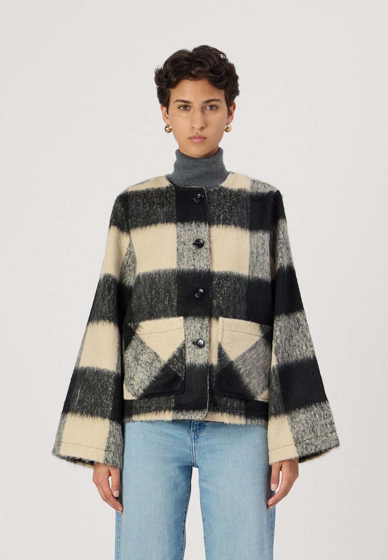 Veste en polaire avec un motif à carreaux noir et crème, dotée d'un col rond, de longues manches évasées, de cinq boutons et de deux poches avant.