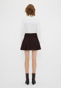 Jupe mini plissée noire à taille haute avec fermeture éclair. Associée à un chemisier blanc avec des accents de boutons sur les manches.