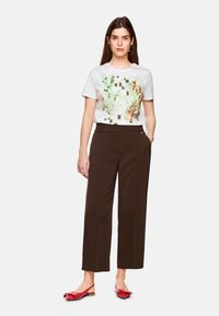 White t-shirt with floral graphic design, paired with dark brown wide-leg trousers and red flats featuring a bow accent.