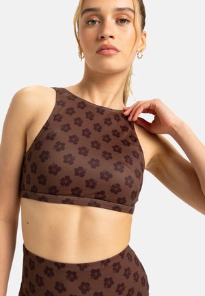 Brun blommig mönstrad crop top med hög halsringning och skurna sidor. Tillverkad av ett mjukt tyg med en figurnära design som framhäver det blommiga mönstret.