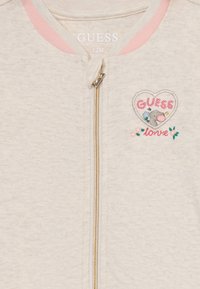 Hellgraue Zip-Jacke aus Bio-Baumwolle. Merkmale sind rosa Akzente, ein herzförmiger Aufnäher mit besticktem Text und ein Elefantendesign.