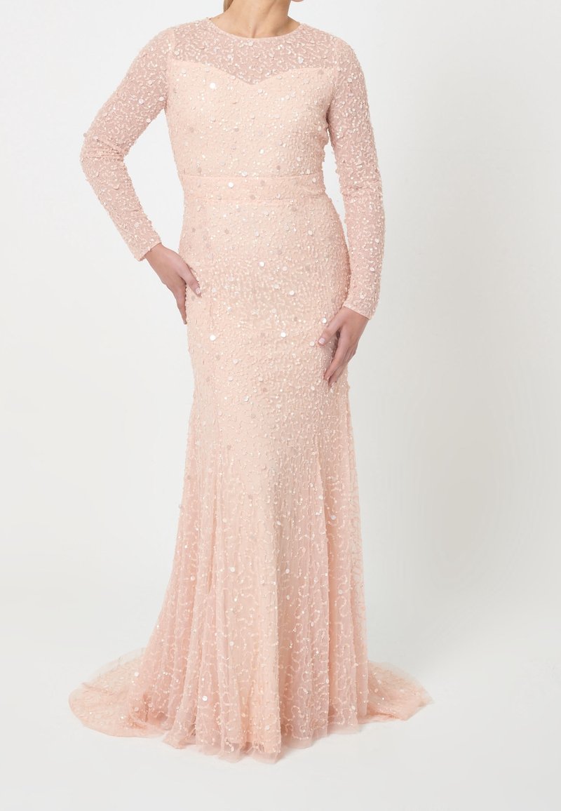 Femme portant une robe longue rose pâle à manches longues, ornée de paillettes, cintrée à la taille et aux hanches, s'évasant légèrement à l'ourlet.