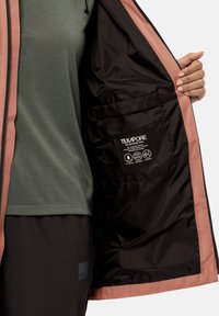 Giacca impermeabile con un guscio esterno rosa chiaro, foderata in nero, e una tasca con etichetta TEXAPORE ECO per la specifica del materiale.
