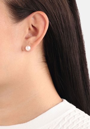 Pendientes de perla redonda en un acabado suave, posados sobre un tono de piel claro con cabello oscuro, que presentan un diseño simple y elegante.