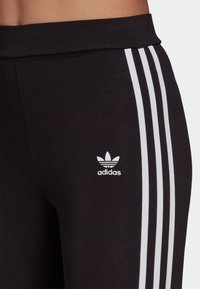 Black athletic pants with a soft texture, featuring three vertical white stripes along the side and a small white adidas logo on the thigh.