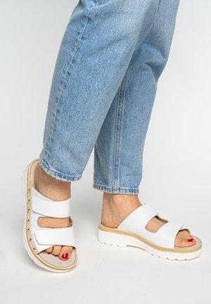 Feet wearing white open-toe sandals with double straps and red nail polish, paired with light blue denim jeans.