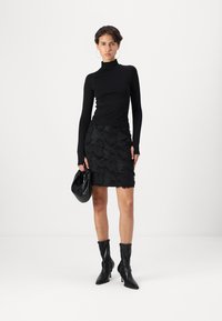 Black turtleneck top paired with a black skirt featuring textured, layered fabric. Black knee-high heeled boots and a small handbag complete the look.