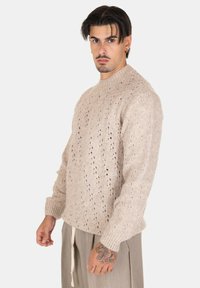 Maglione lavorato a maglia beige chiaro con scollo rotondo, motivo testurizzato e maniche lunghe, caratterizzato da dettagli in pizzo e polsini a costine.