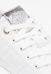 Baskets blanches avec lacets blancs, détail perforé sur le côté et patch argenté métallique sur la languette avec marquage en relief.