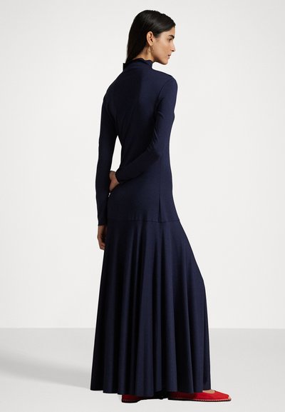 Vestido de manga larga en color azul marino con falda acampanada, que presenta un cuello alto y un diseño elegante. Combinado con unos zapatos de un rojo brillante, que muestran una textura de tela suave.