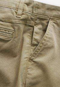 Pantaloni in cotone beige con zip, tasche frontali inclinati e una tasca posteriore con dettagli di cucitura sottili.