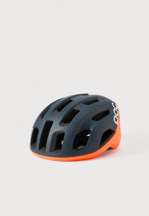 Un casque de cyclisme gris foncé avec des fentes d’aération, une coque inférieure orange vif et des inscriptions blanches, sur un fond uni.