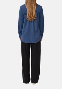 Chemise en coton texturé bleu à manches longues avec un ourlet arrondi, associée à un pantalon noir à jambes larges avec des poignets côtelés.
