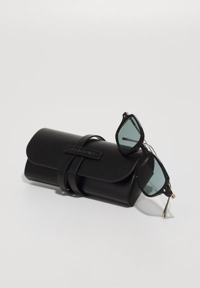 Schwarze Sonnenbrillen mit blauen getönten Gläsern liegen neben einem schwarzen Lederetui mit einem Tragegurt und eingeprägtem Markennamen.