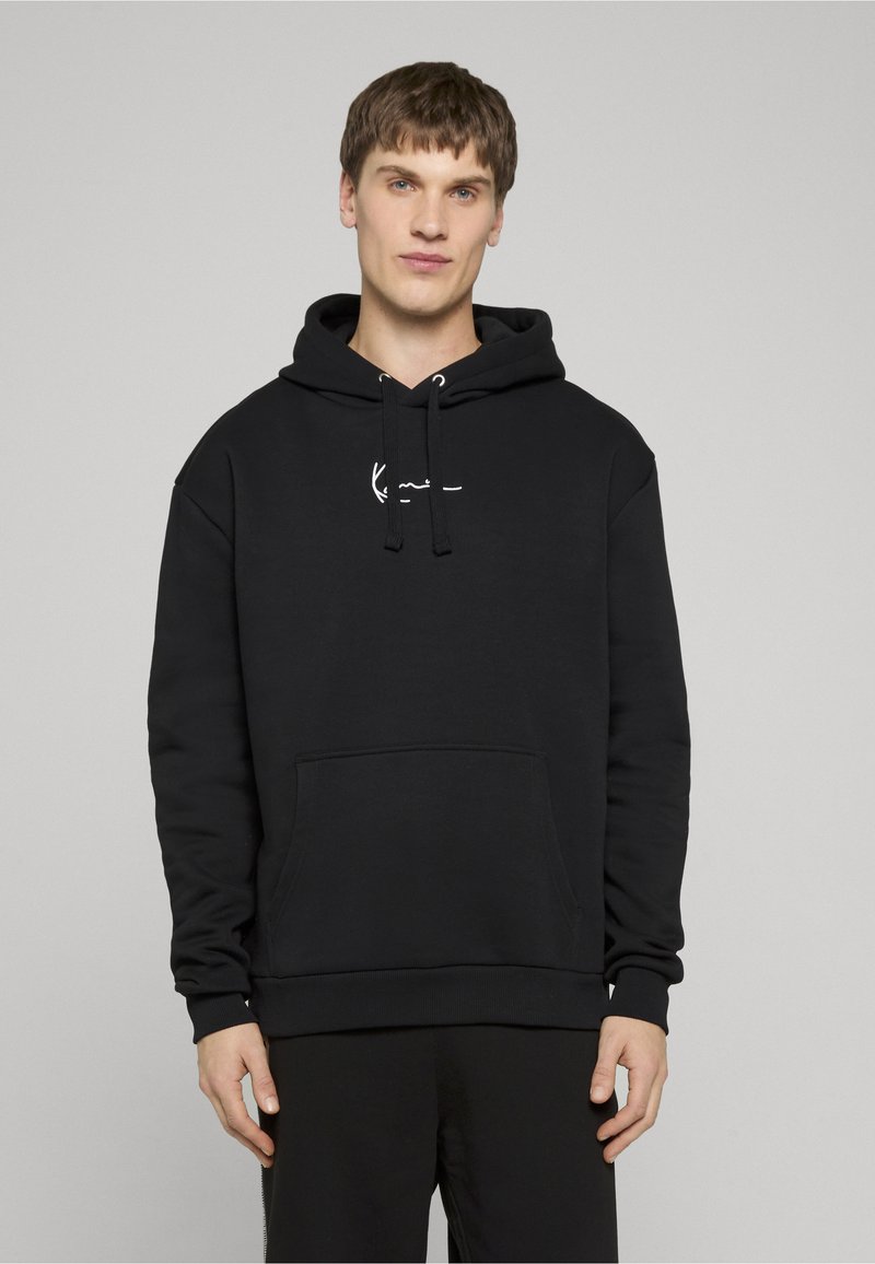 Sweat à capuche noir en tissu doux, doté d'une poche frontale, d'une capuche avec cordon de serrage, et d'un logo blanc sur la poitrine. Design simple et décontracté.