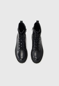 Bottines en cuir noir avec une finition lisse, devant à lacets, fermeture éclair sur le côté et semelle en caoutchouc robuste. Comprend une languette pour un enfilage facile.