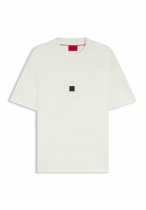 Cream-colored t-shirt, short sleeves, round neck, featuring embossed logo on the chest, and a rectangular black accent. Soft jersey fabric.
