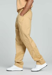 Beige, leichte Hose mit elastischem Bund und Seitentaschen; verfügt über ein gerades Bein-Design und eine glatte Textur. Getragen mit weißen Turnschuhen.