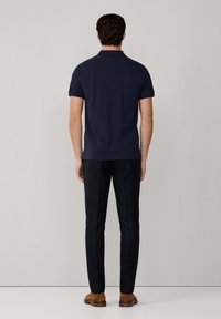 Marinblå polo skjorta med korta ärmar och krage, kombinerad med mörka byxor och bruna skor. Tyget verkar slätt och åtsittande.