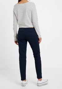 Pruhovaný dlouhý rukáv v krémové a navy barvě, spárovaný s navy slim-fit kalhotami. Bílé tenisky s černými akcenty dokončují outfit.