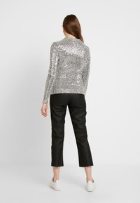 Silberner Paillettenoberteil mit langen Ärmeln, Rundhalsausschnitt und tailliertem Design, kombiniert mit schwarzen Caprihosen und weißen Sneakers.