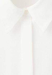 Gros plan d'une chemise blanche à col mettant l'accent sur le col pointu et la zone du bouton supérieur.