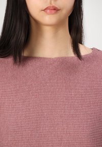 Texturerad rosa tröja med båthals. Tyget har smala vertikala ribbor och ett mjukt, stickat utseende.