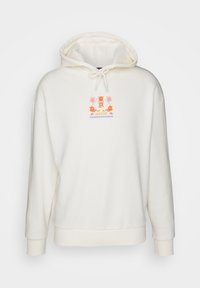 Off-white huvtröja med dragsko, med liten färgglad text "Tokyo Japan" och drakgrafik centrerad på bröstet.