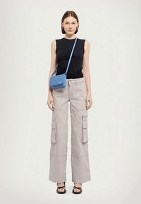 Musta hihaton paita, vaaleanharmaat leveälahkeiset cargo-housut taskuilla ja pieni sininen olkalaukku säädettävällä hihnalla. Mustat sandaalit.