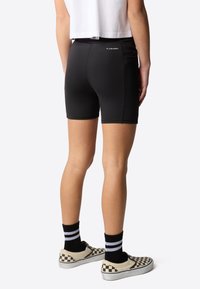 Svarta.idrottsshorts med en åtsittande design, slät textur och 'FLASHDRY'-märke ovanför midjan, i kombination med rutiga slip-on skor.