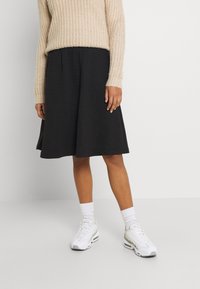 Černá, strukturovaná sukně ve tvaru A s vaflovým vzorem. V kombinaci s béžovým pleteným svetrem a bílými teniskami, doplněné bílými ponožkami.