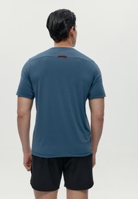 Majica kratkih rukava za sport u tamnoplavoj tkanini, s suptilnim crvenim detaljem na stražnjoj strani. Lagana, glatka tekstura i prilagođeni kroj.