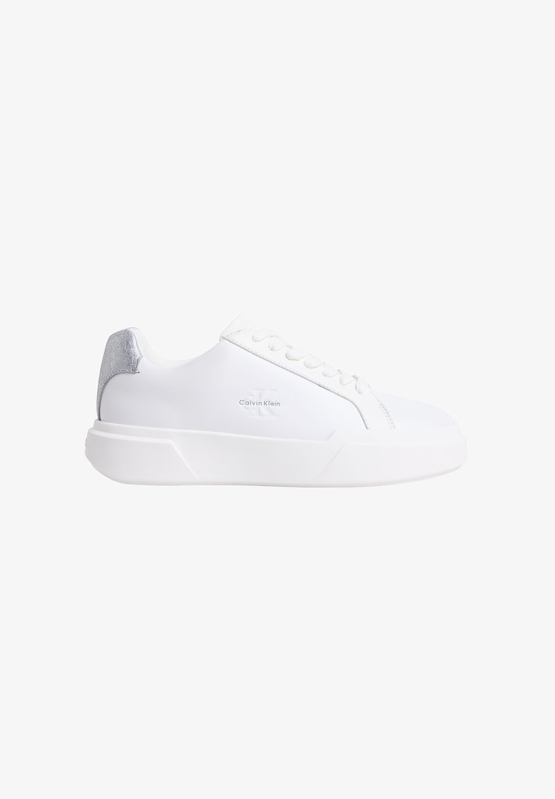 Witte Calvin Klein lage sneaker met dikke zool en zilveren hielaccent, zijaanzicht tegen een witte achtergrond.
